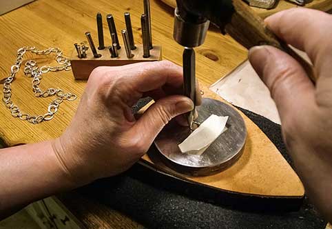 image of a jewelers bench with jeweler stamping a hallmark onto a piece of precious gold