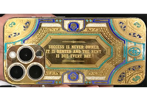 a gold bi-metal phone case engraved with enameling and a quote "success is never owned, it is rented and the rent is due everyday"